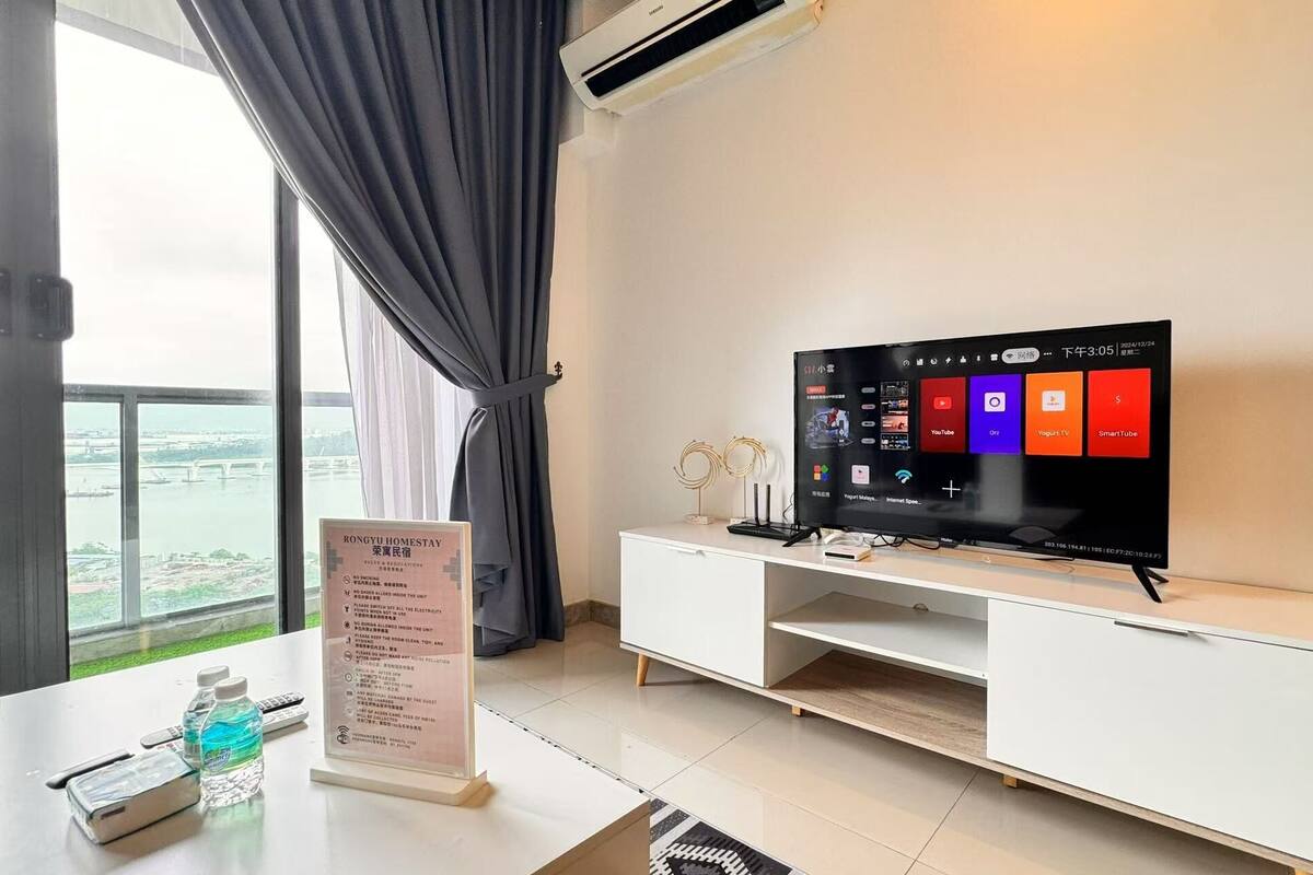 A modern hotel room with a large window, a flat-screen TV, a white entertainment unit, and a sign with rules.