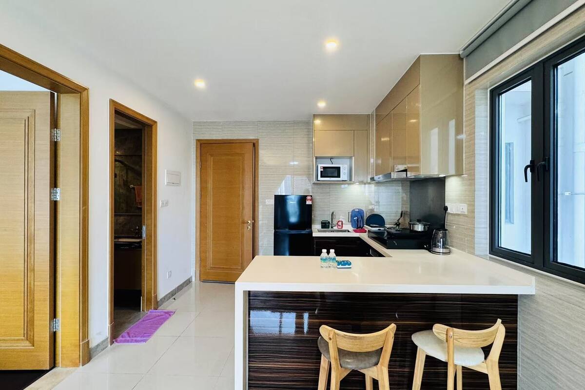 A modern kitchen with a central island, wooden cabinets, and a large window.