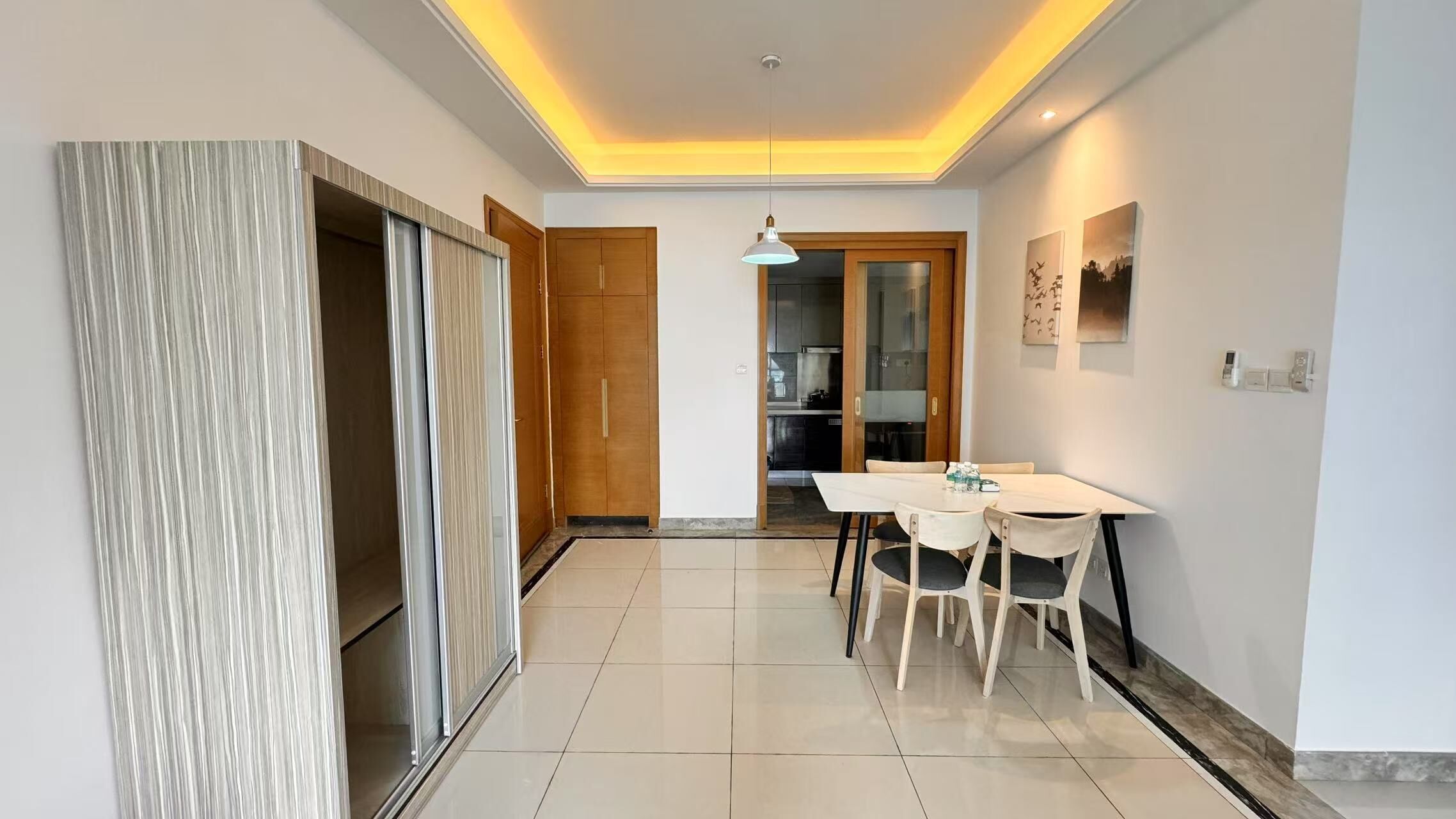 A modern interior with a dining area, a kitchen in the background, and a hallway leading to a door.