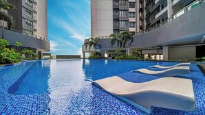 Ein moderner Hotelpool mit klarem, blauem Wasser, umgeben von Hochhäusern und Palmen.