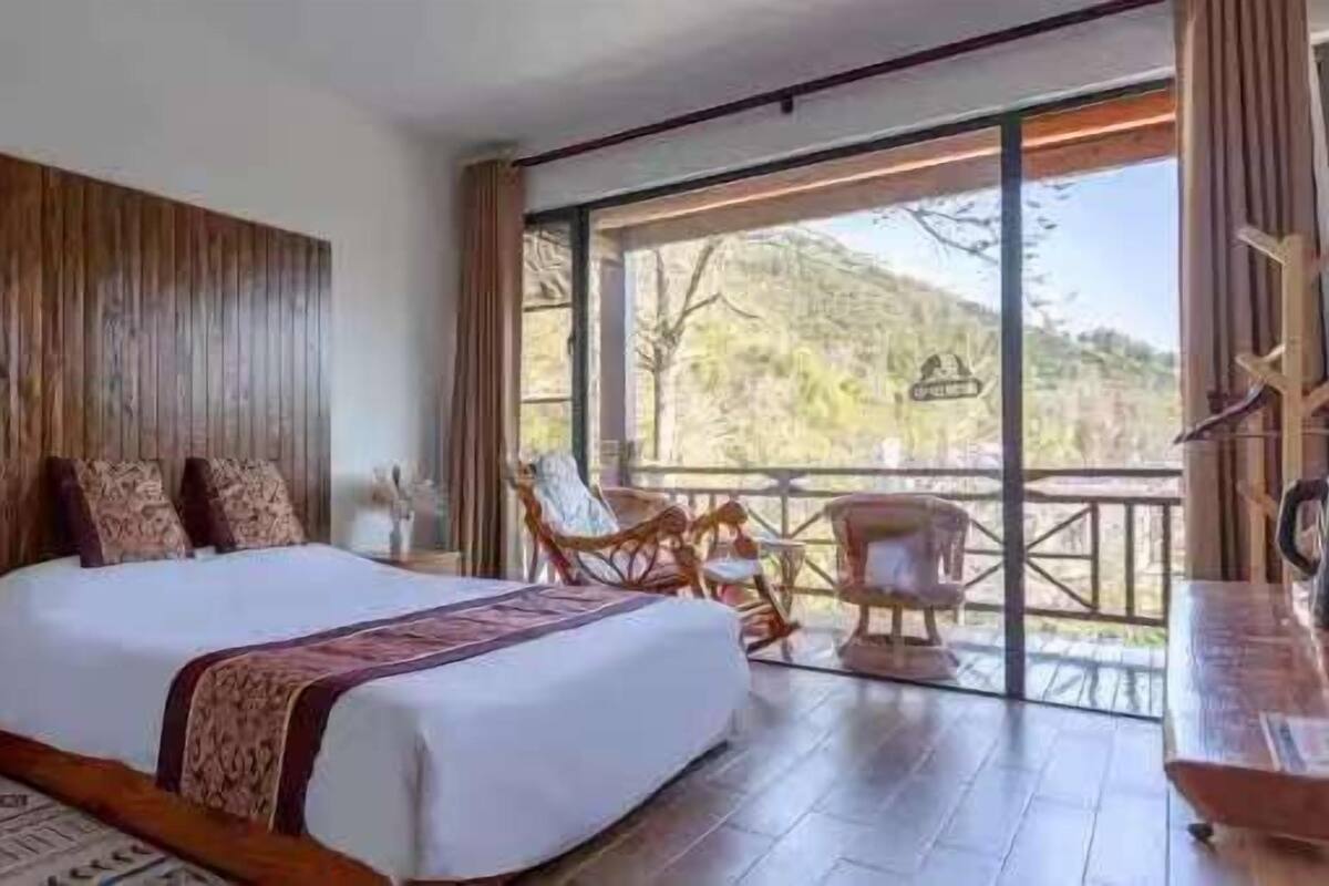Ein Schlafzimmer mit einem großen Bett, einem Holzkopfende, einem Nachttisch, einem Schreibtisch mit Stuhl und einem Balkon mit Korbmöbeln.
