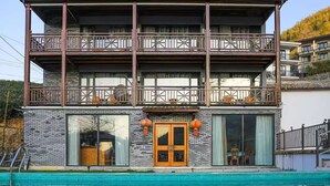 A multi-story building with a balcony, large windows, and a swimming pool in front.