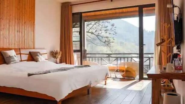 A bedroom with a large bed, wooden headboard, and a view of a mountain through a sliding door.