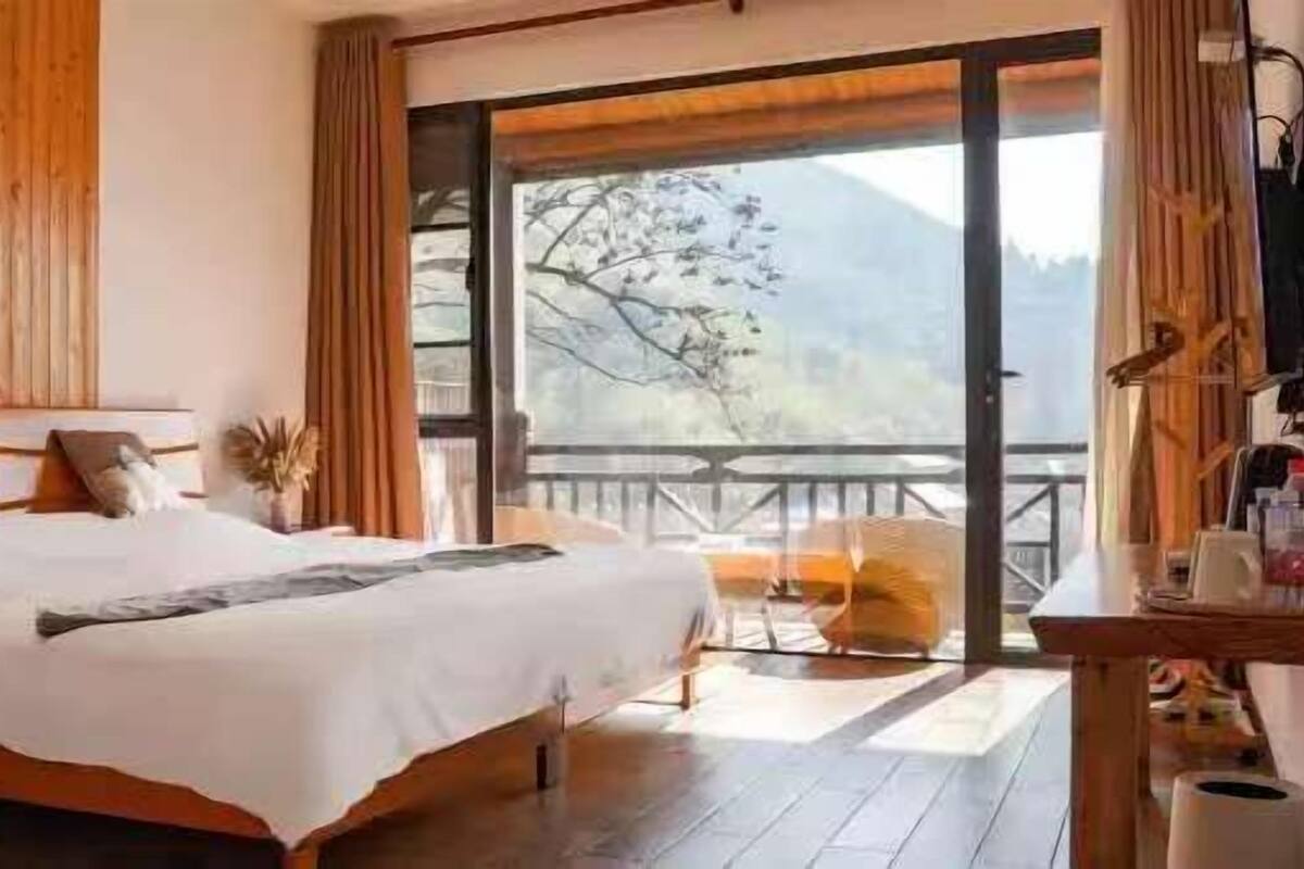 Ein Schlafzimmer mit einem großen Bett, einem Holzkopfende und Bergblick durch eine Schiebetür.