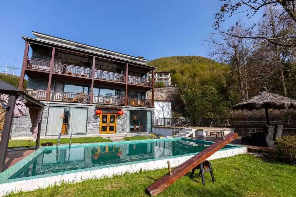 Ein zweistöckiges Gebäude mit Pool, Au ßenbereich und einem Reetdachhaus.