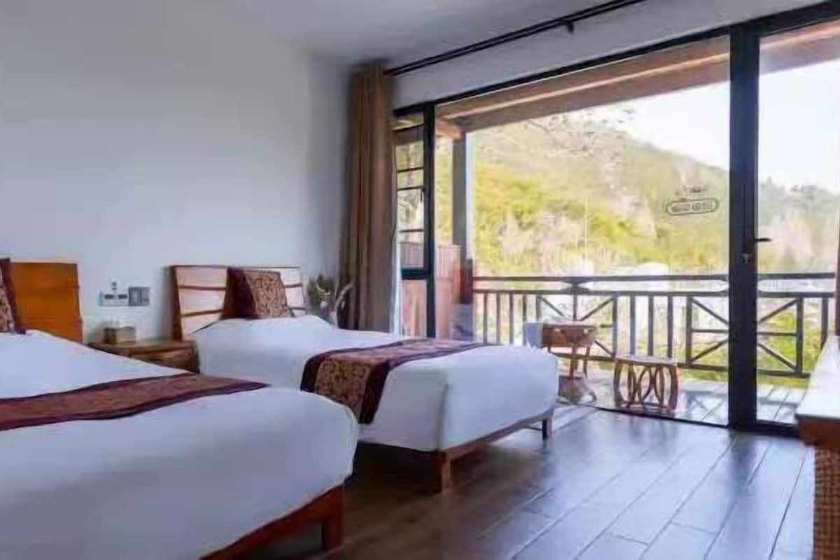 Ein Zimmer mit zwei Betten, einem Balkon mit Blick ins Freie und einem Holzboden.