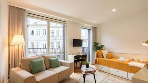 Quarto de hotel moderno com sofá, mesa pequena, TV e varanda com vista para a cidade.