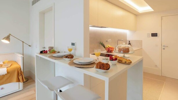 Quarto moderno e bem iluminado com espaço para o café da manhã, incluindo frutas, pão e um copo de suco de laranja.