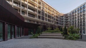 Um edifício moderno com vários andares, grandes janelas e um pátio central com escadas e vegetação.