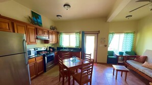 A compact kitchen with wooden cabinets, a refrigerator, stove, and a dining table with chairs. - Sea View Cabana@SapphireBeachResort (Not available)
