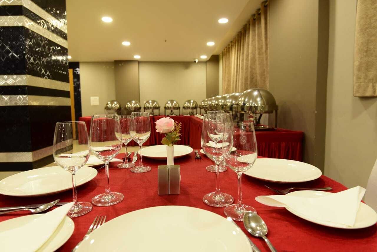 Une table à manger dressée avec de l’argenterie blanche, des verres à vin et des couverts, et un vase rempli de fleurs roses placé au centre.
