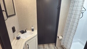A compact bathroom with a toilet, sink, and shower area. - Cozy RV Retreat with Private Hot Tub and Fenced Yard (Spring Hill)