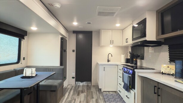 A compact RV kitchen with a dining area, a microwave, stove, and cabinets. - Cozy RV Retreat with Private Hot Tub and Fenced Yard (Spring Hill)