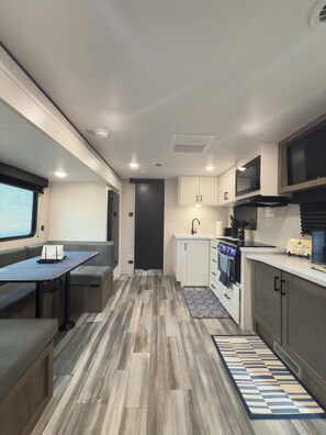 A compact RV kitchen with a dining area, a microwave, stove, and cabinets. - Cozy RV Retreat with Private Hot Tub and Fenced Yard (Spring Hill)