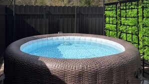 A round hot tub with a wicker exterior, surrounded by a wooden fence, under string lights. - Cozy RV Retreat with Private Hot Tub and Fenced Yard (Spring Hill)