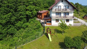 A two-story house with a balcony, surrounded by lush greenery and a playground.