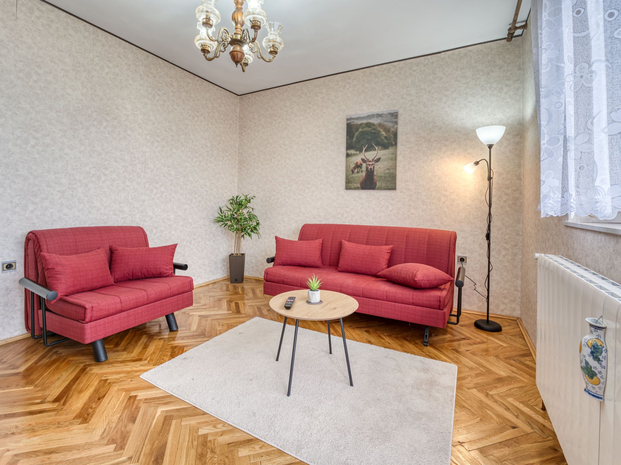 A living room with two red sofas, a small round table, a potted plant, and a chandelier.