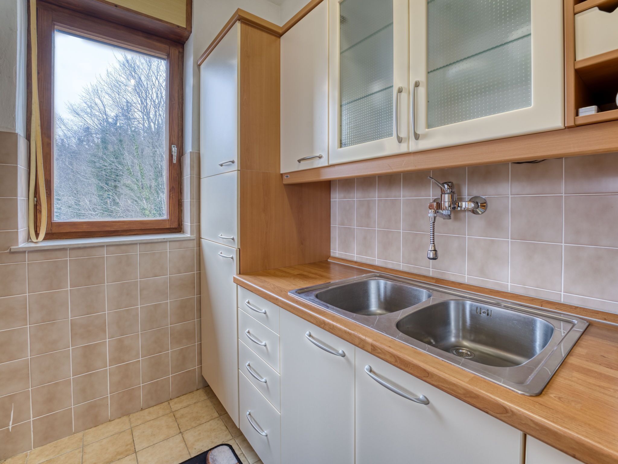 A kitchen with two stainless steel sinks, a window, and white cabinets.