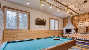 Een pooltafel in een ruimte met houten wanden en een stenen open haard.
