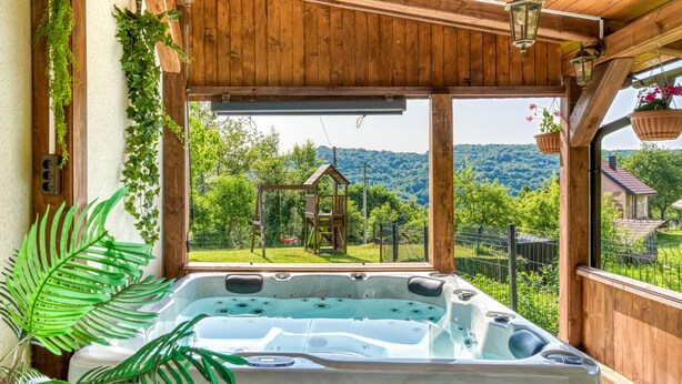 Een houten terras met een jacuzzi, een houten pergola en uitzicht op een tuin en bergen.