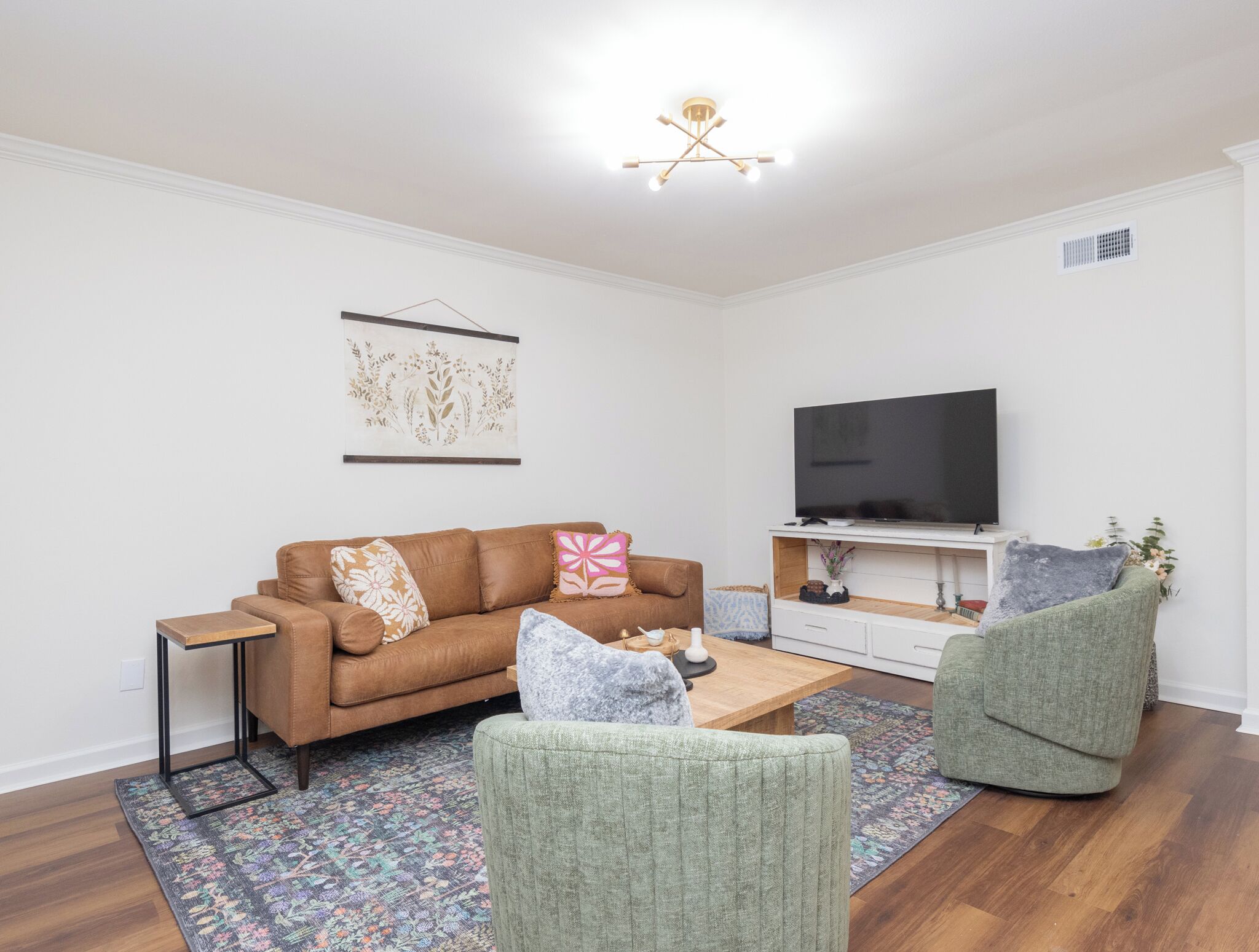 A modern living room with a brown sofa, a green armchair, a coffee table, and a flat-screen TV on a white stand.