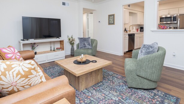 Ein modernes Wohnzimmer mit einem Flachbildfernseher, einem Holztisch und grünen Sesseln.