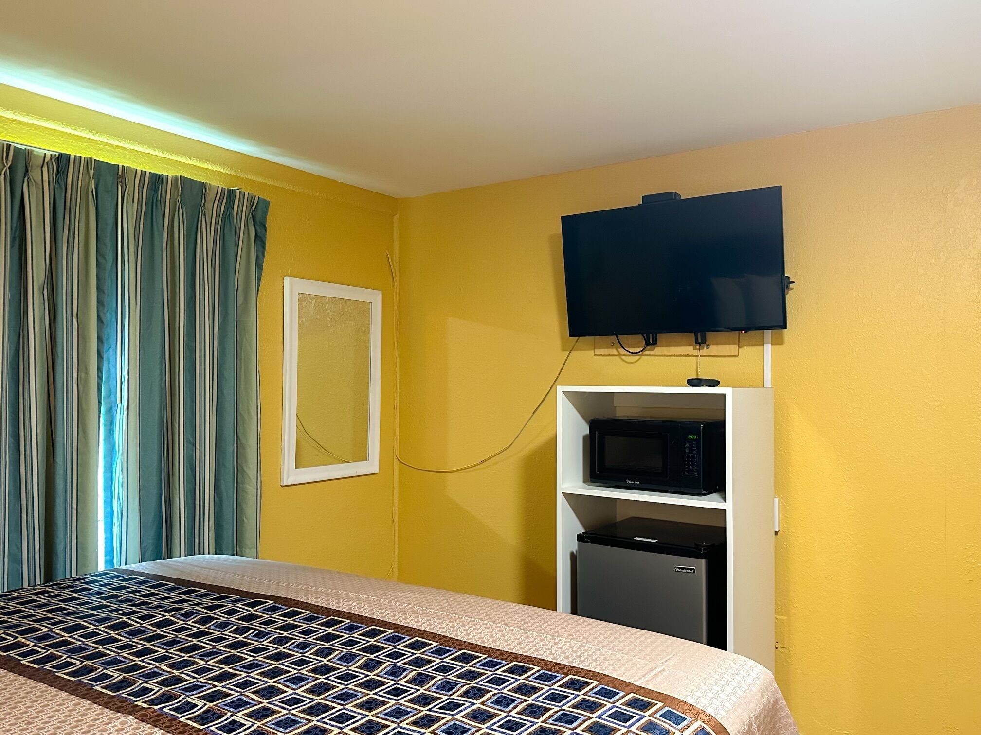 Une chambre équipée d’un lit, d’un téléviseur fixé au mur, d’un four à micro-ondes et d’un petit réfrigérateur.