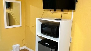Een compacte kamer met een gele wand, een wandgemonteerde flatscreen-tv, een magnetron en een minibar.