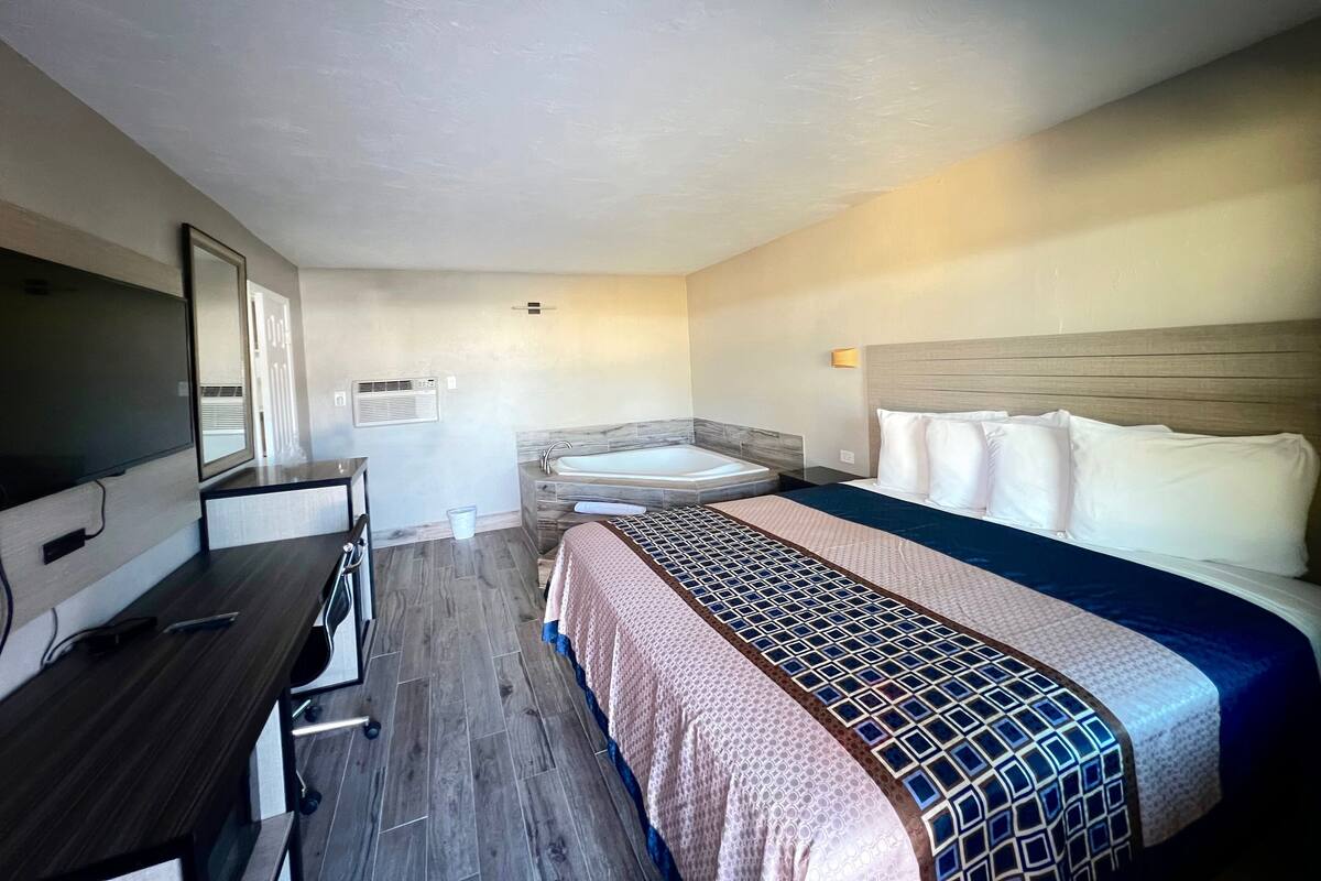Quarto de hotel com cama, secretária, televisão, banheiro com banheira e espelho.