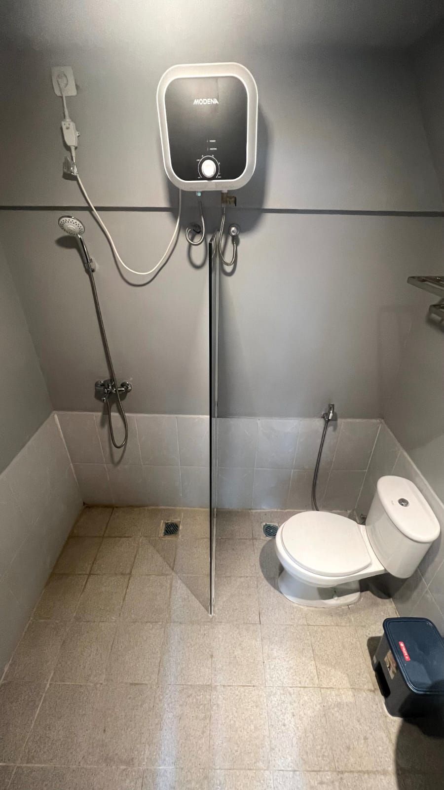 A small, tiled bathroom with a toilet, shower, and a wall-mounted control panel.