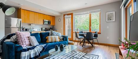 A modern living room with a blue sofa, a coffee table, and a dining area with chairs and a table.
