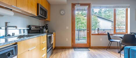 Una cocina moderna con armarios de madera, electrodomésticos de acero inoxidable y un amplio ventanal con vistas a un balcón.