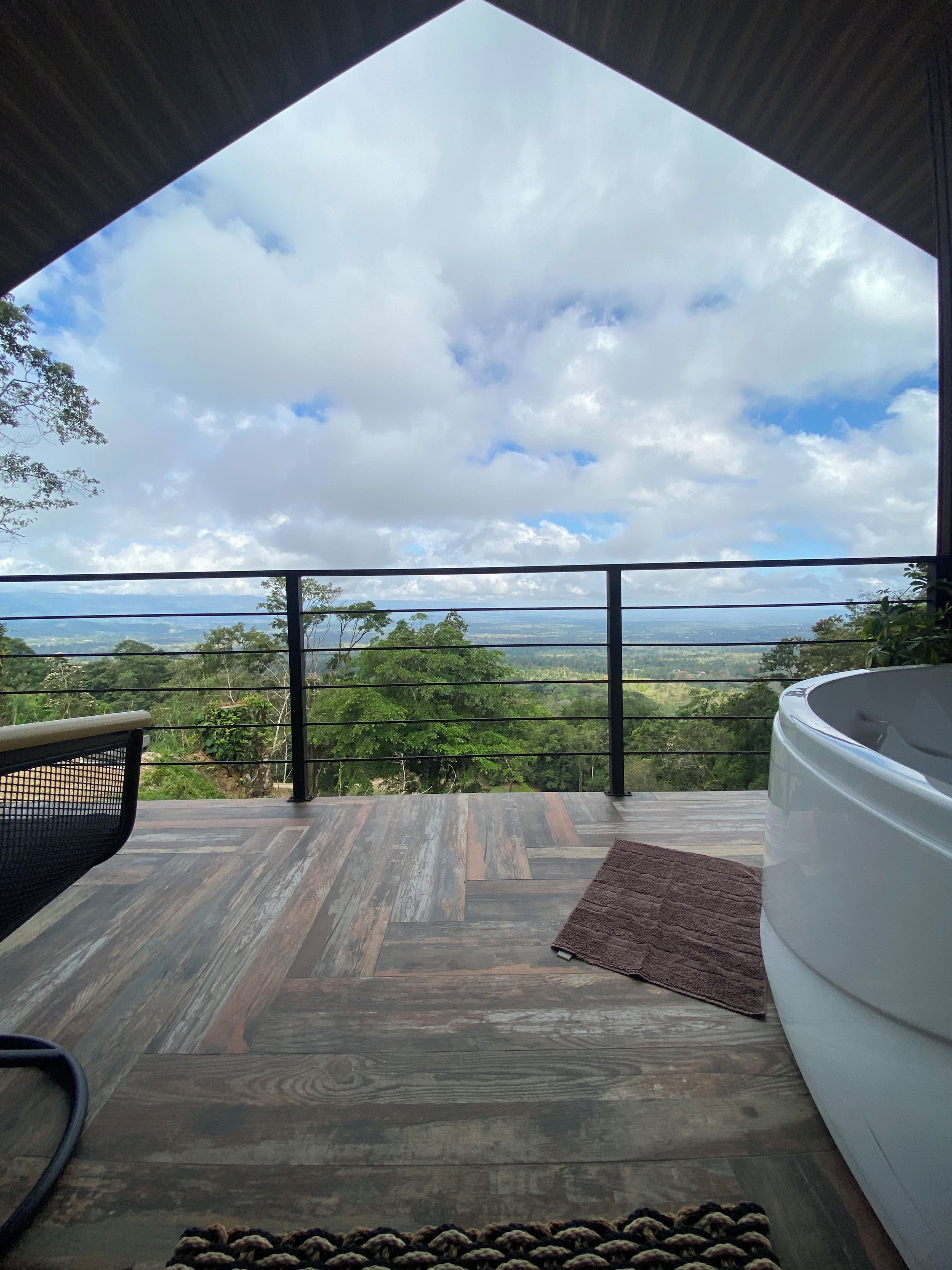 Una habitación con vistas a un paisaje a través de un ventanal grande, piso de madera y una bañera blanca.