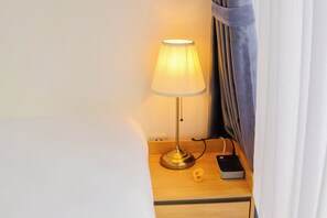 A bedside table with a lamp, a power strip, and a small device, likely a phone charger. - Otia Villa by Premier Hospitality Asia (Nusa Dua)