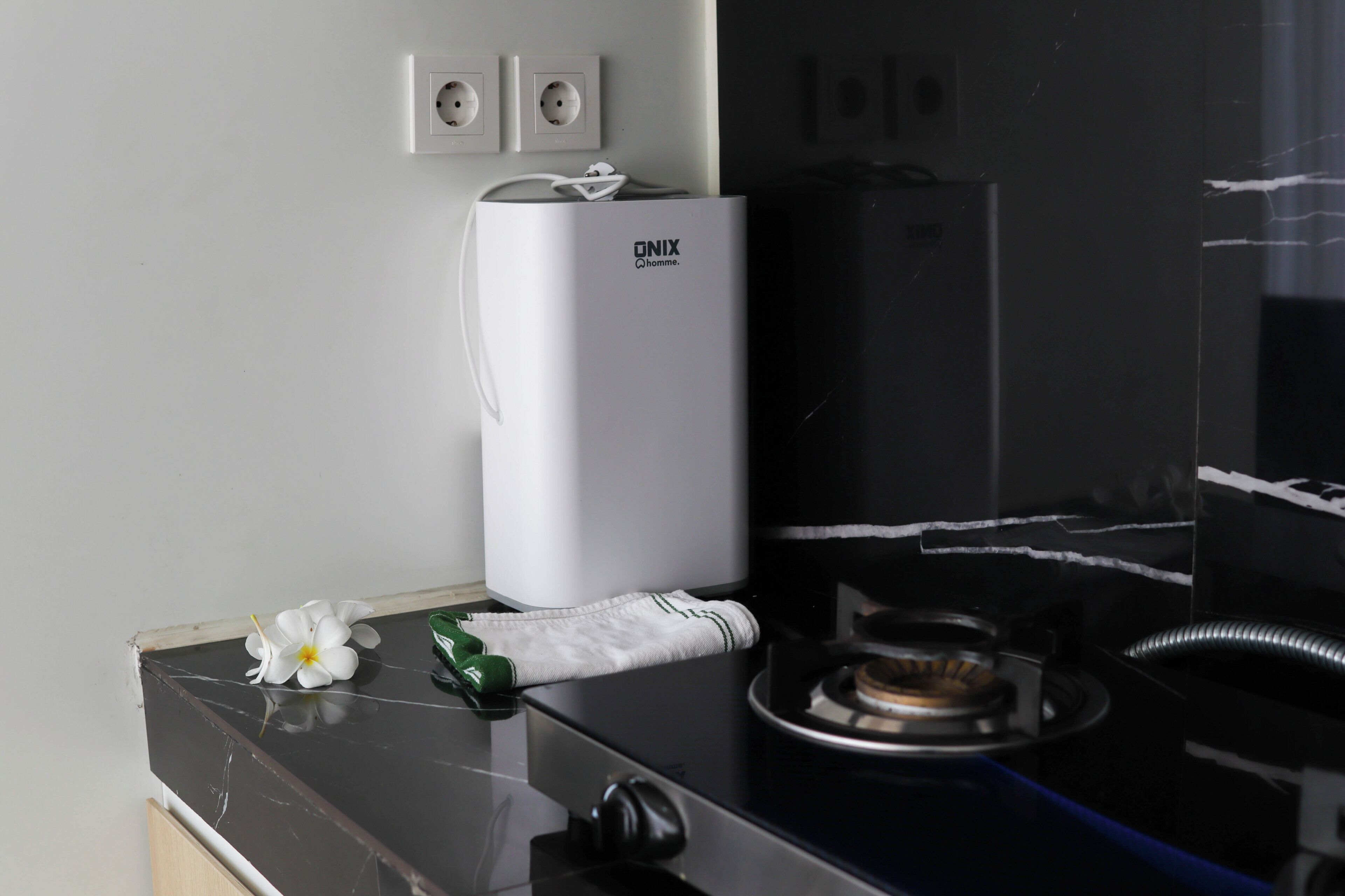 A kitchen with a black countertop, a white water dispenser, a green towel, and a white flower.