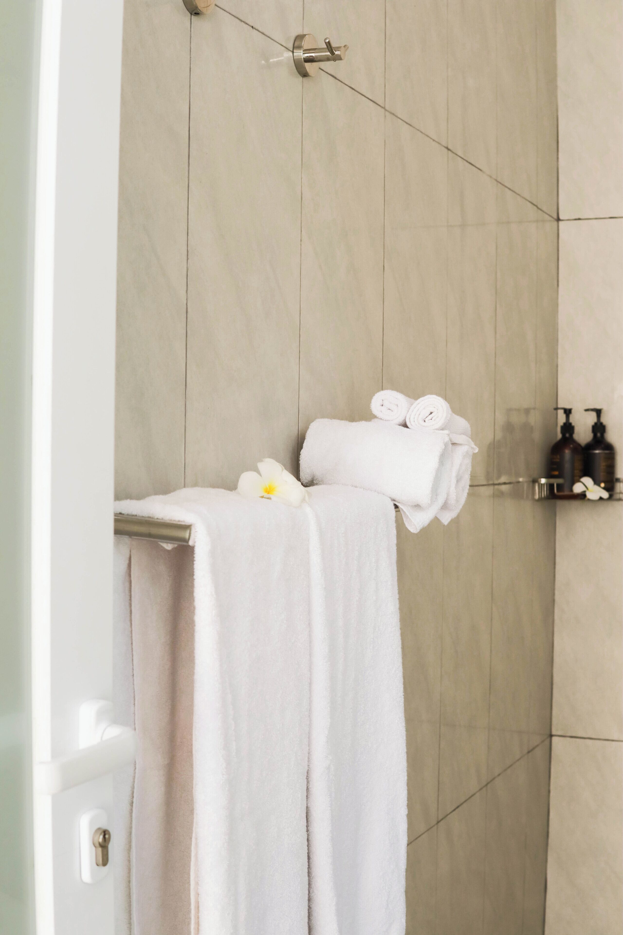 A bathroom with a towel rack holding rolled towels, a flower, and toiletries on a shelf.