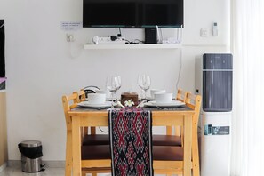 A dining table set with white plates, glasses, and cutlery, a small decorative item, and a patterned cloth draped over the chair backs.