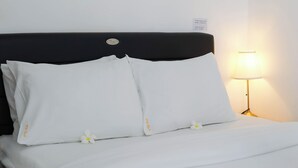 A bed with white bedding and pillows, a nightstand with a lamp, and a wall-mounted label. - Otia Villa by Premier Hospitality Asia (Nusa Dua)