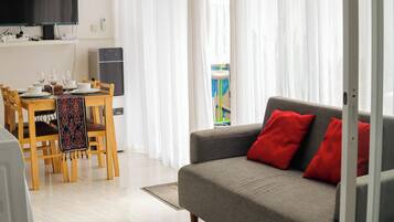 Een moderne woonkamer met een grijze bank en rode kussens, een eethoek met houten stoelen en een tafel, en een grote flatscreen televisie aan de muur.