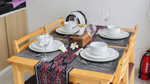 A dining table set with white plates, glasses, and a wooden box, with a patterned table runner. - Otia Villa by Premier Hospitality Asia (Nusa Dua)