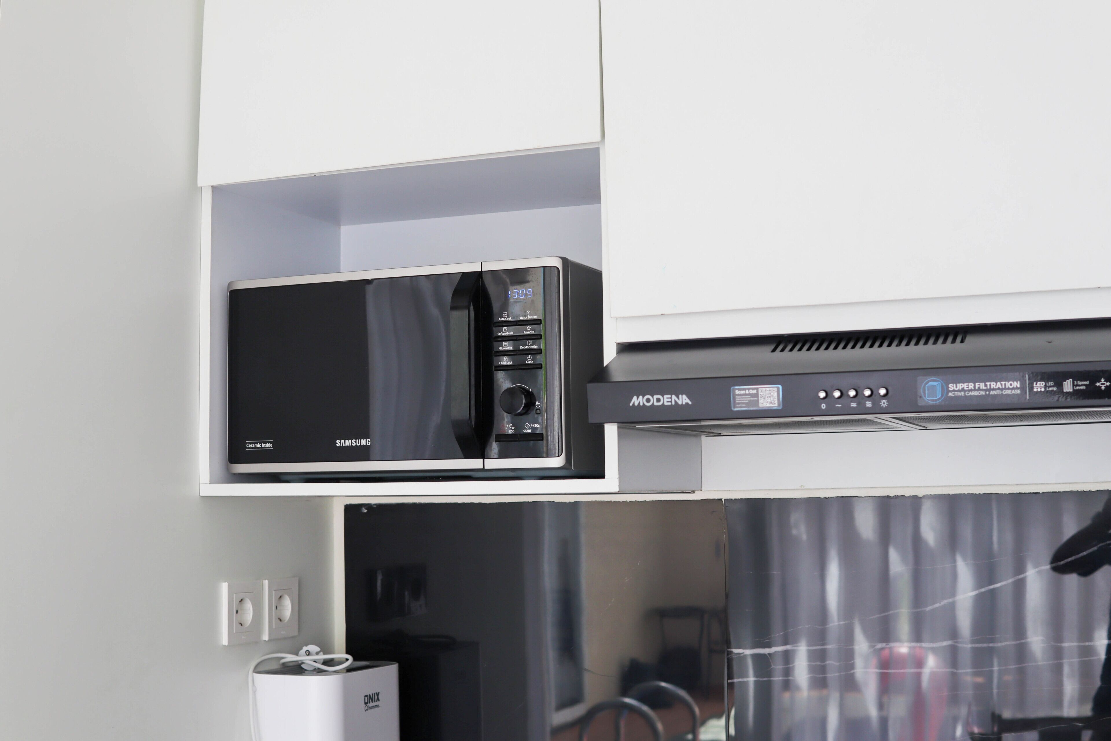 A microwave oven with a digital display and a control panel, placed on a white shelf above a white cabinet.