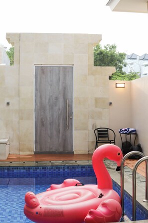 Ein Swimmingpool mit einem rosa Flamingo-Schwimmpflege, einer Tür und einem kleinen Tisch mit einem Stuhl.