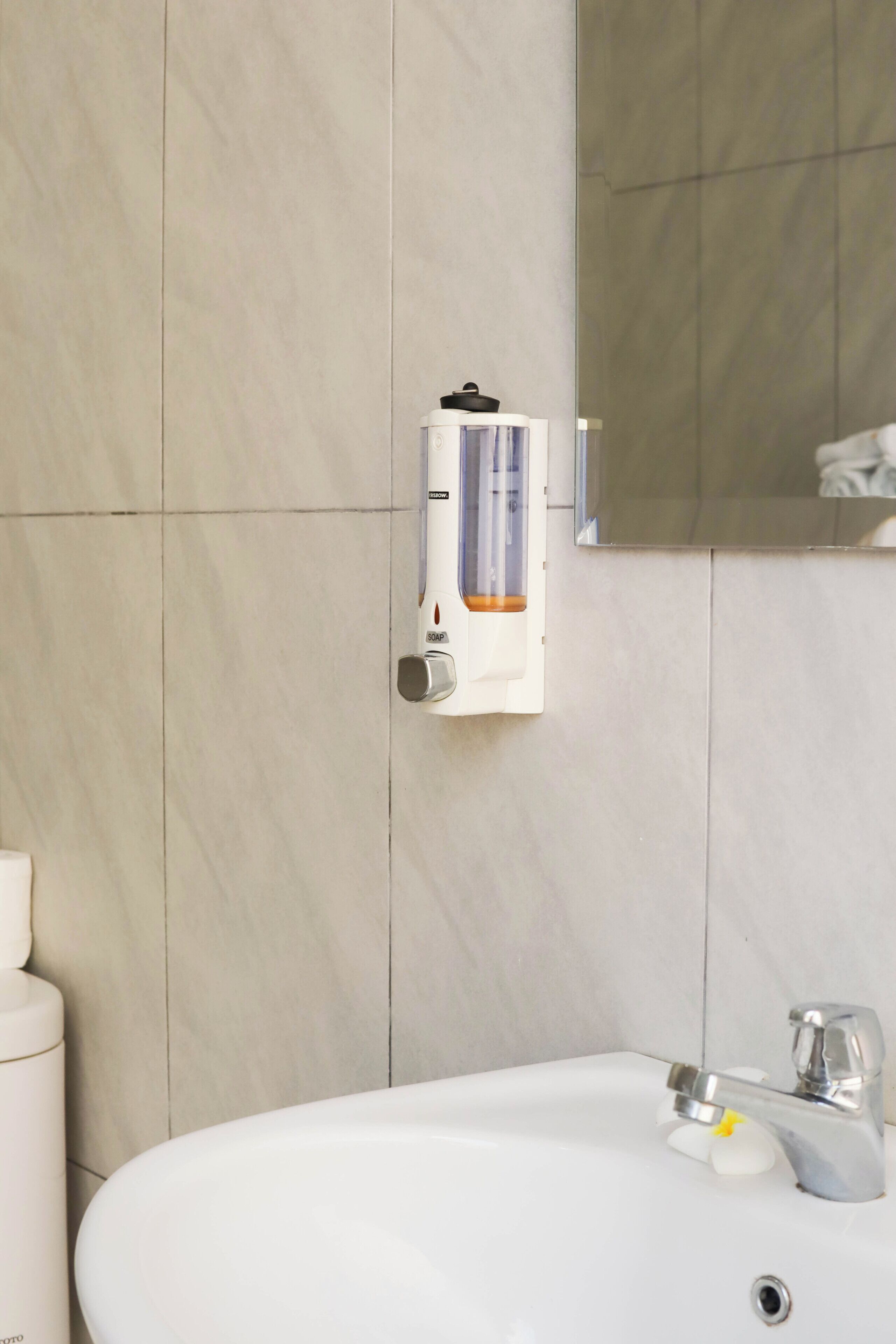 Une salle de bain avec un lavabo blanc, un miroir et un distributeur de savon fixé au mur.