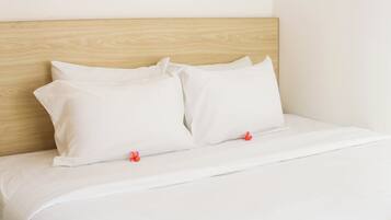 A neatly made bed with white bedding and pillows, a wooden headboard, and a small red flower on the pillow.