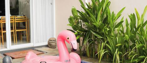 A pink inflatable flamingo by a pool with a tiled edge, surrounded by green plants.
