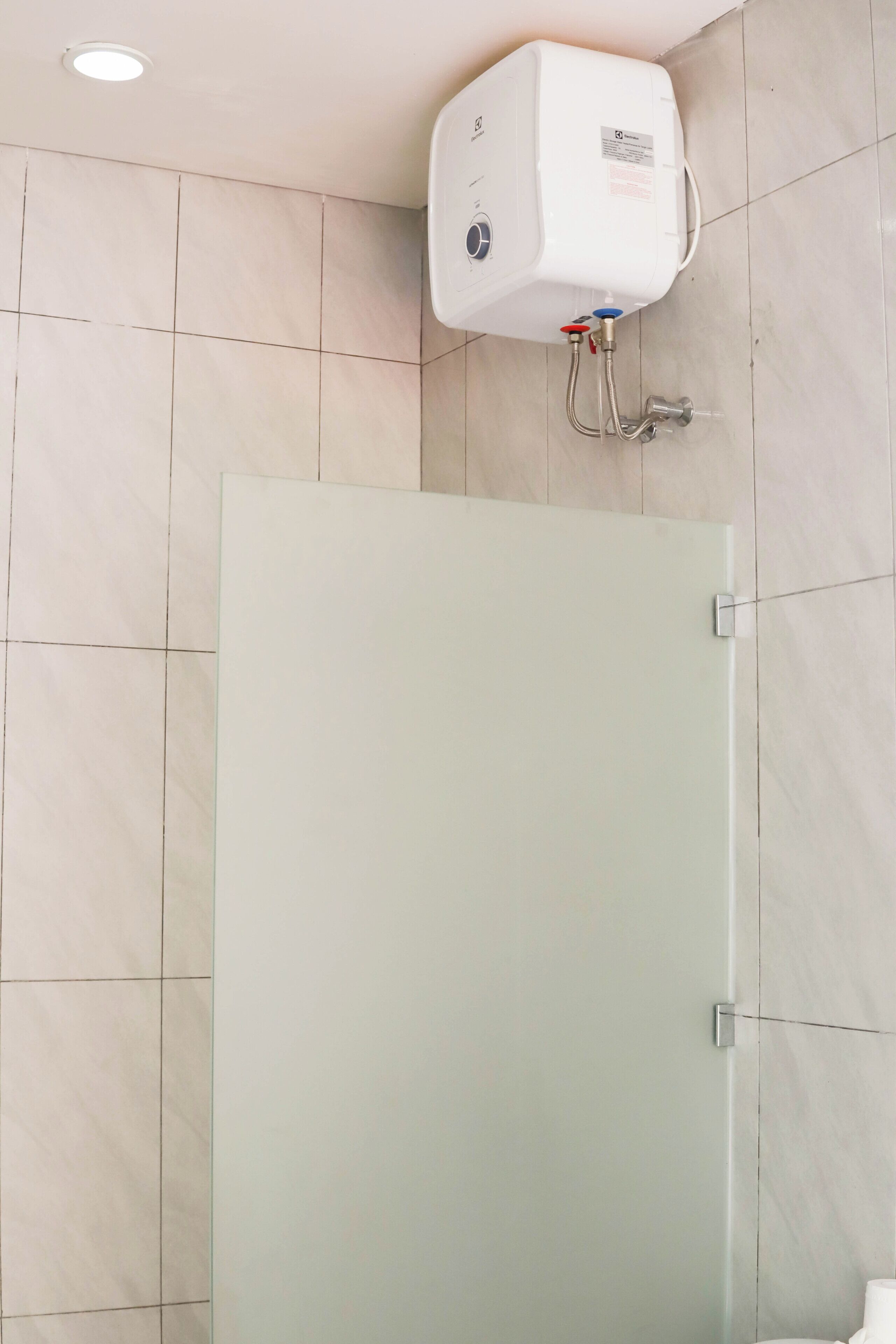 A bathroom with a glass shower door, a white water heater mounted on the wall, and a tiled floor.