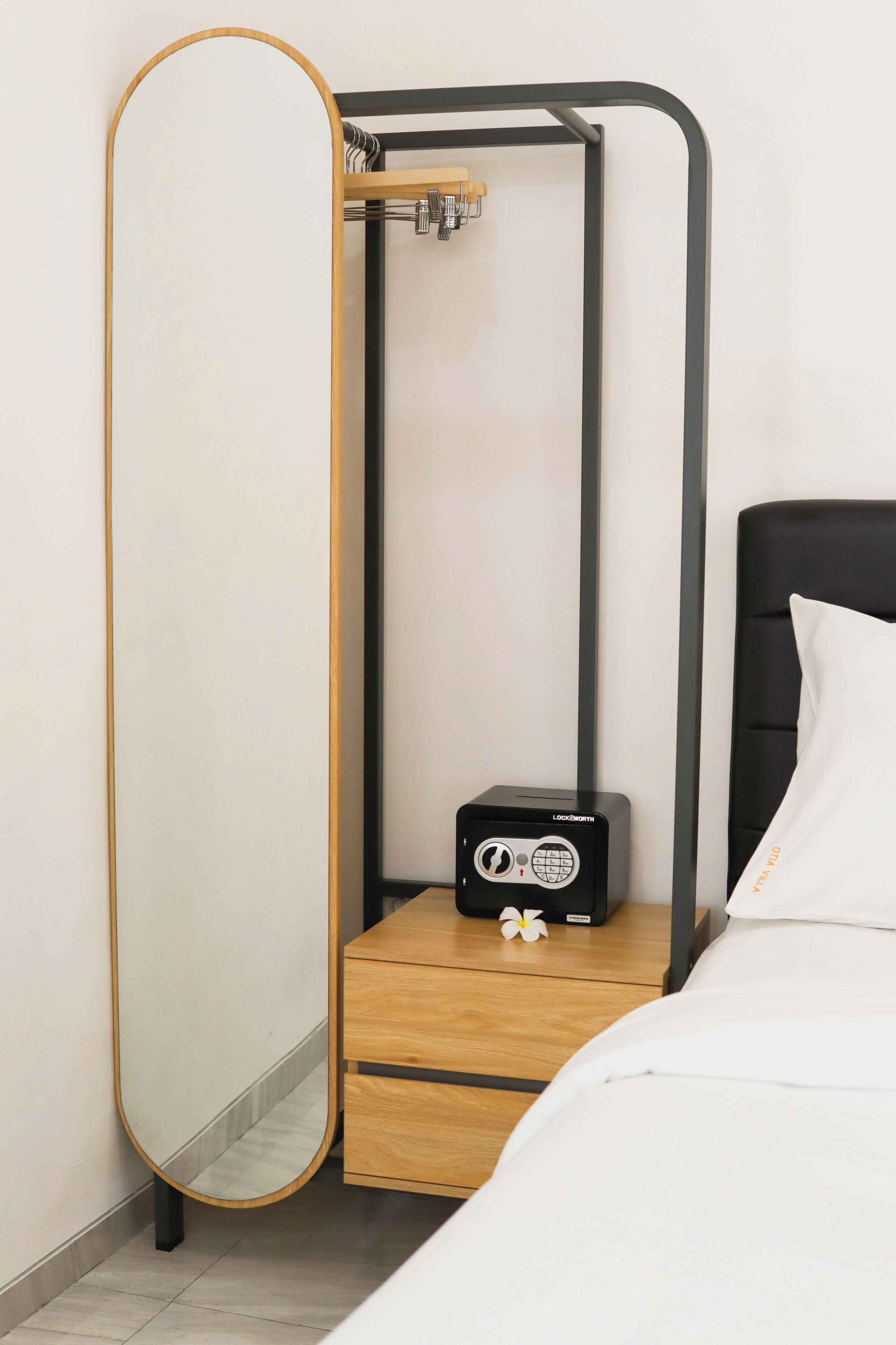 A bedroom with a bed, a nightstand, a mirror, and a small black device on the nightstand.