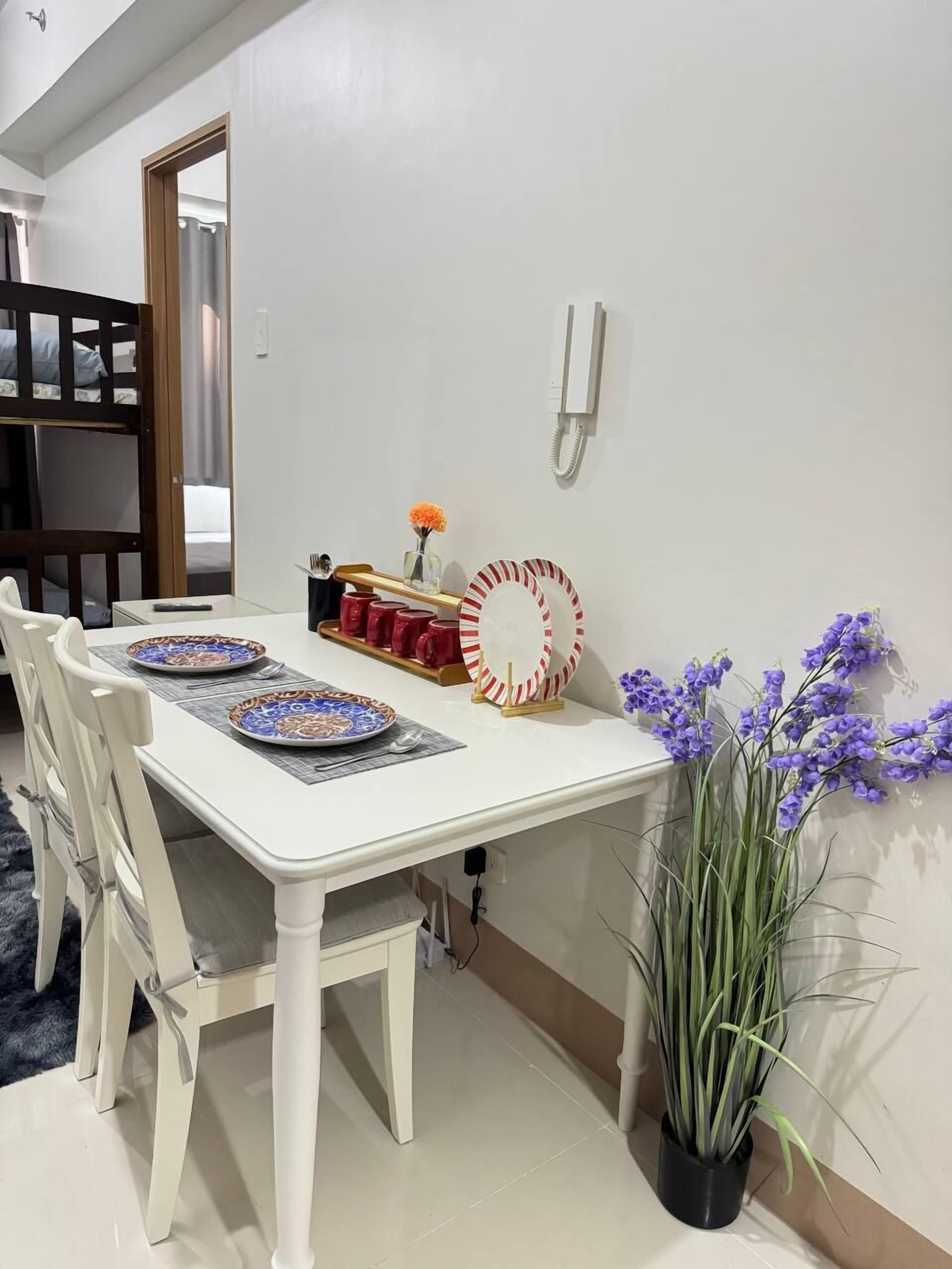 A dining area with a white table, red and white striped plates, and a potted plant with purple flowers.