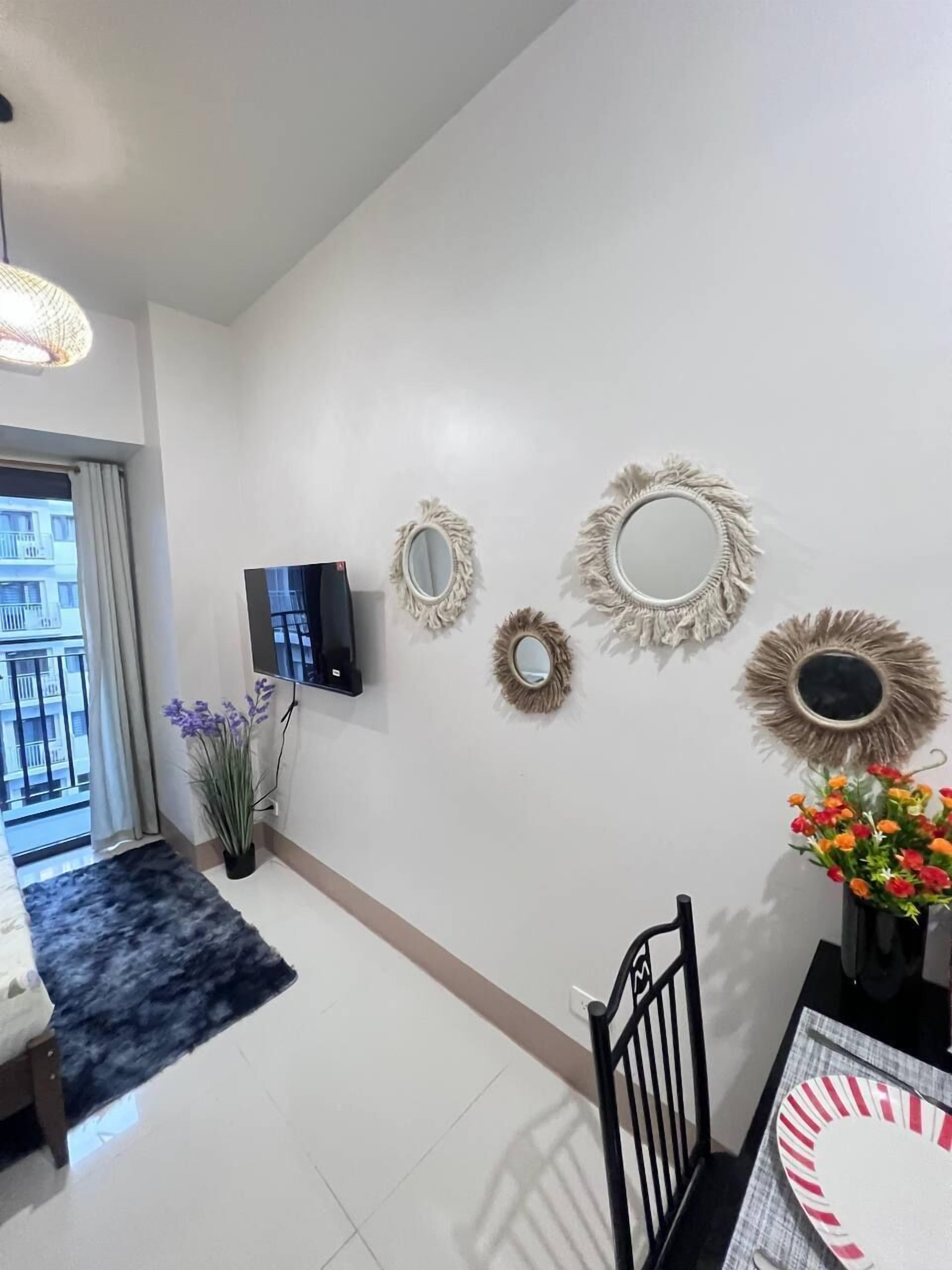 A modern living room with a flat-screen TV, decorative wall mirrors, a potted plant, and a dining area with a table and chairs.