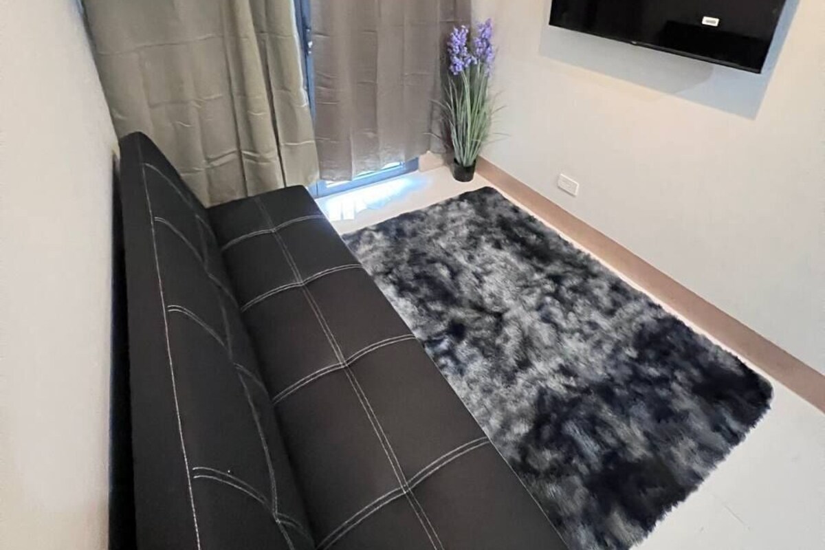A modern living room with a black sofa, a mounted TV, and a window with curtains.